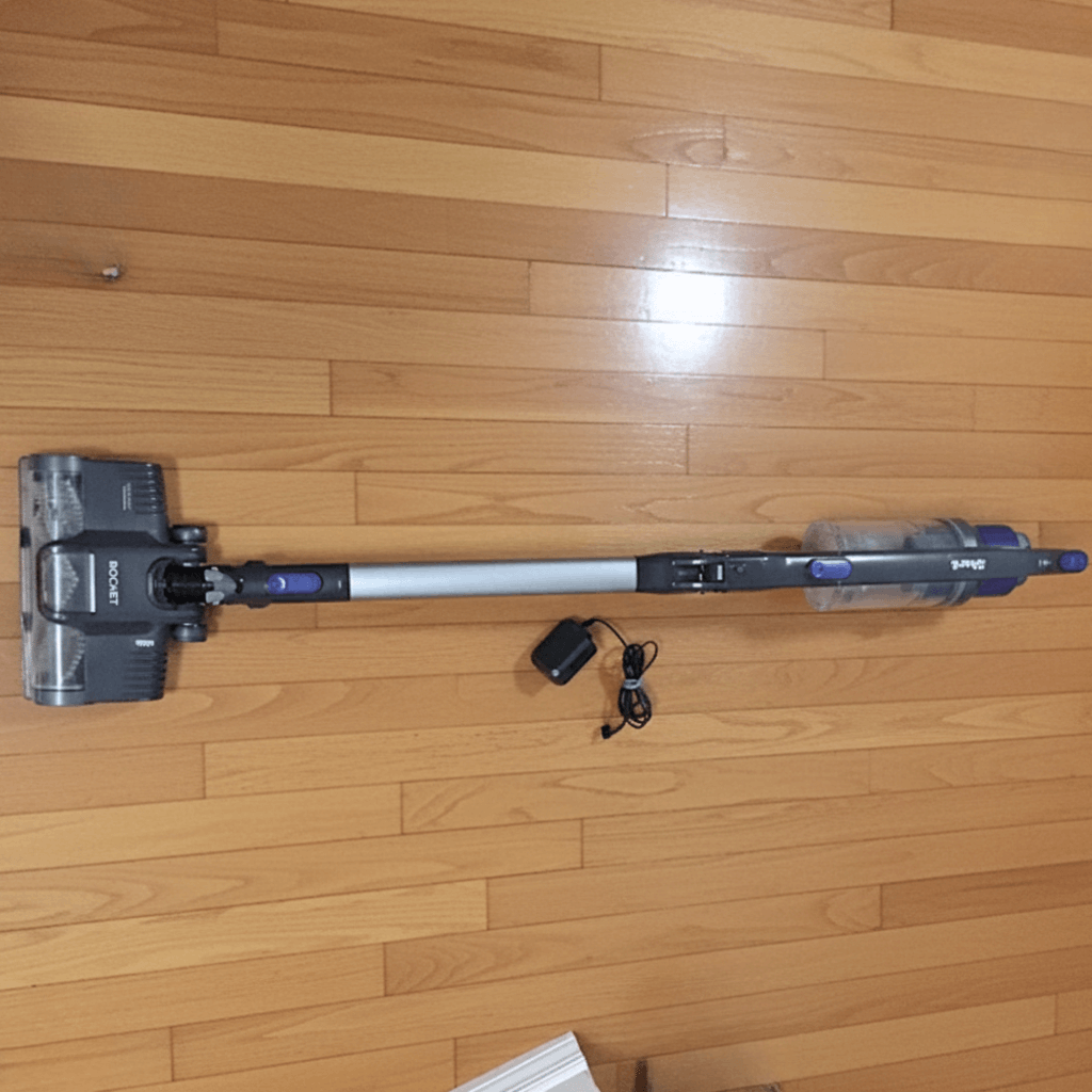 Overhead view of a Shark Rocket IX141 cordless stick vacuum cleaner laying flat on a wood floor next to its charging adapter.